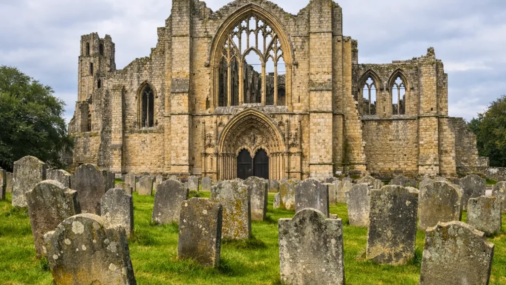 Ancienne abbaye médiévale gothique en pierre dans la campagne anglaise, entourée d’un vieux cimetière aux tombes inclinées couvertes de mousse.