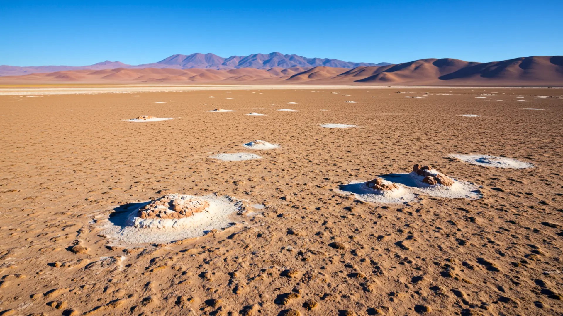 Paysage aride du désert d’Atacama avec sol craquelé, dépôts de sel et montagnes en arrière-plan