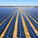 Vue aérienne ultra-réaliste d’une vaste ferme solaire avec des rangées de panneaux photovoltaïques alignées sur un paysage rural sec sous un ciel bleu.