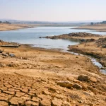 Sol craquelé et niveau d’eau très bas dans un lac asséché, illustrant la sécheresse et la diminution des réserves d’eau douce.