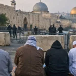 Des fidèles prient à l’aube près des remparts de Jérusalem, devant une zone fermée menant vers Al-Aqsa, sous surveillance à distance.