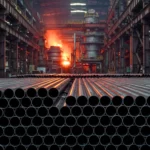 Tubes en acier alignés dans une aciérie avec un haut fourneau en fusion en arrière-plan
