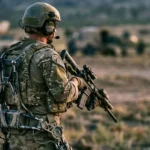 Un soldat équipé d’un exosquelette et d’un casque immersif se tient de dos sur un terrain d’entraînement militaire.