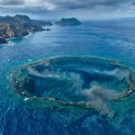 Vue réaliste en plongée aérienne d’une immense caldeira volcanique sous-marine au sud du Japon, visible sous une mer bleu profond près d’îles volcaniques.