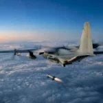 Un avion de transport militaire vole au-dessus d’une épaisse couche nuageuse à l’aube, au moment où une petite fusée commence son allumage.