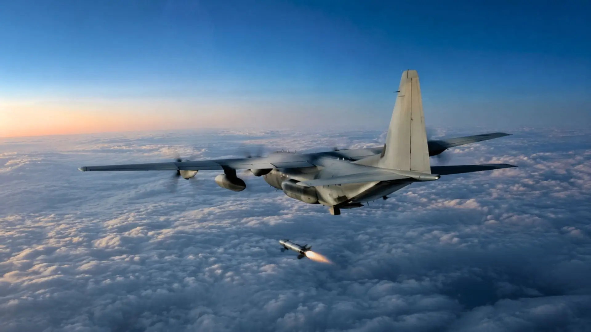 Un avion de transport militaire vole au-dessus d’une épaisse couche nuageuse à l’aube, au moment où une petite fusée commence son allumage.