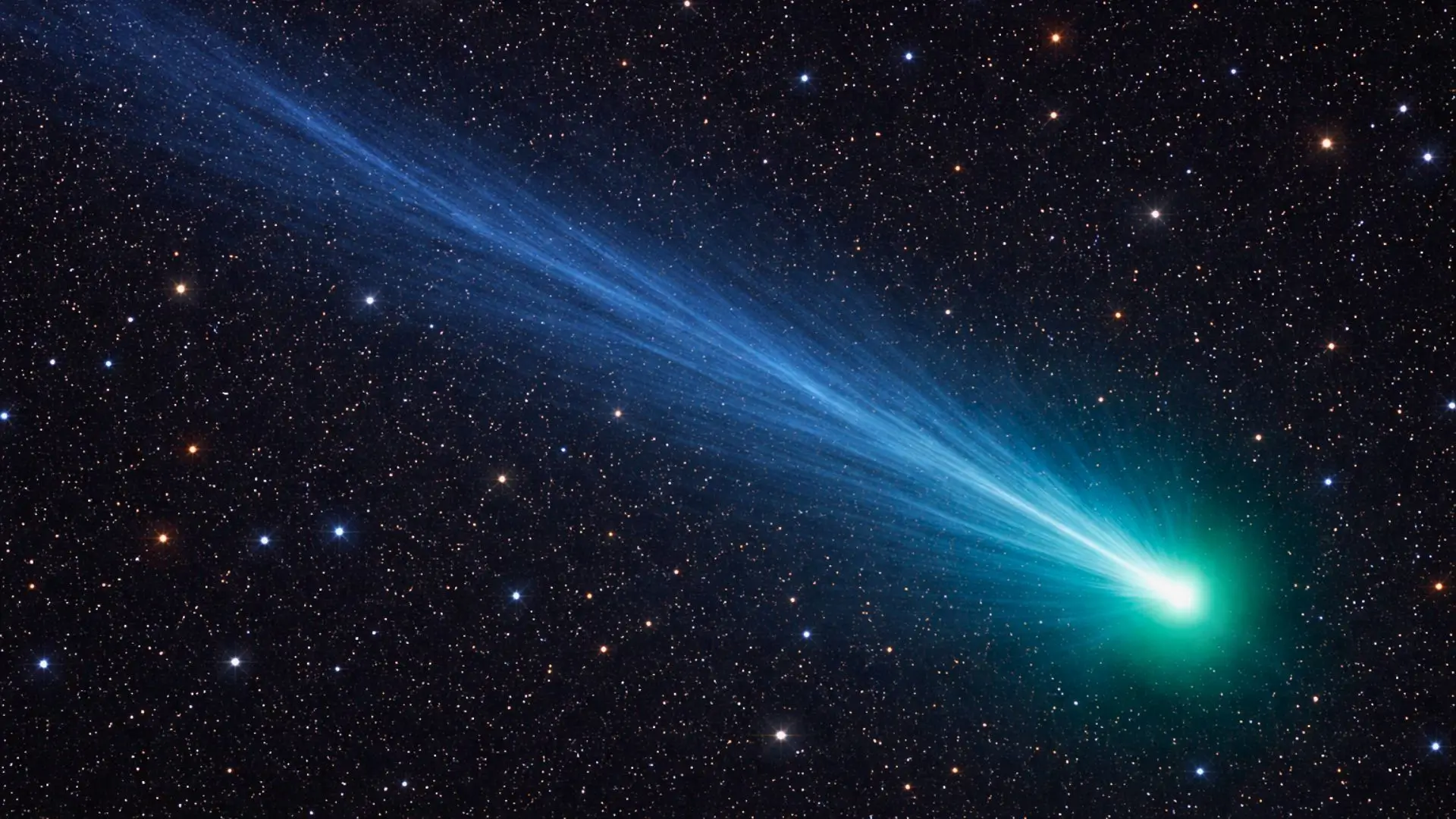 Une comète lumineuse traverse l’espace profond en diagonale, avec une longue queue ionique bleue et une coma vert turquoise sur fond d’étoiles colorées.