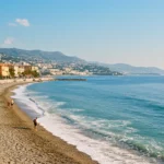 Plage méditerranéenne paisible avec ville côtière et mer calme illustrant le risque caché de tsunami