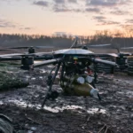 Un lourd drone hexacoptère militaire ukrainien est posé dans une position de front boueuse à l’aube, avec des munitions visibles sous sa structure.