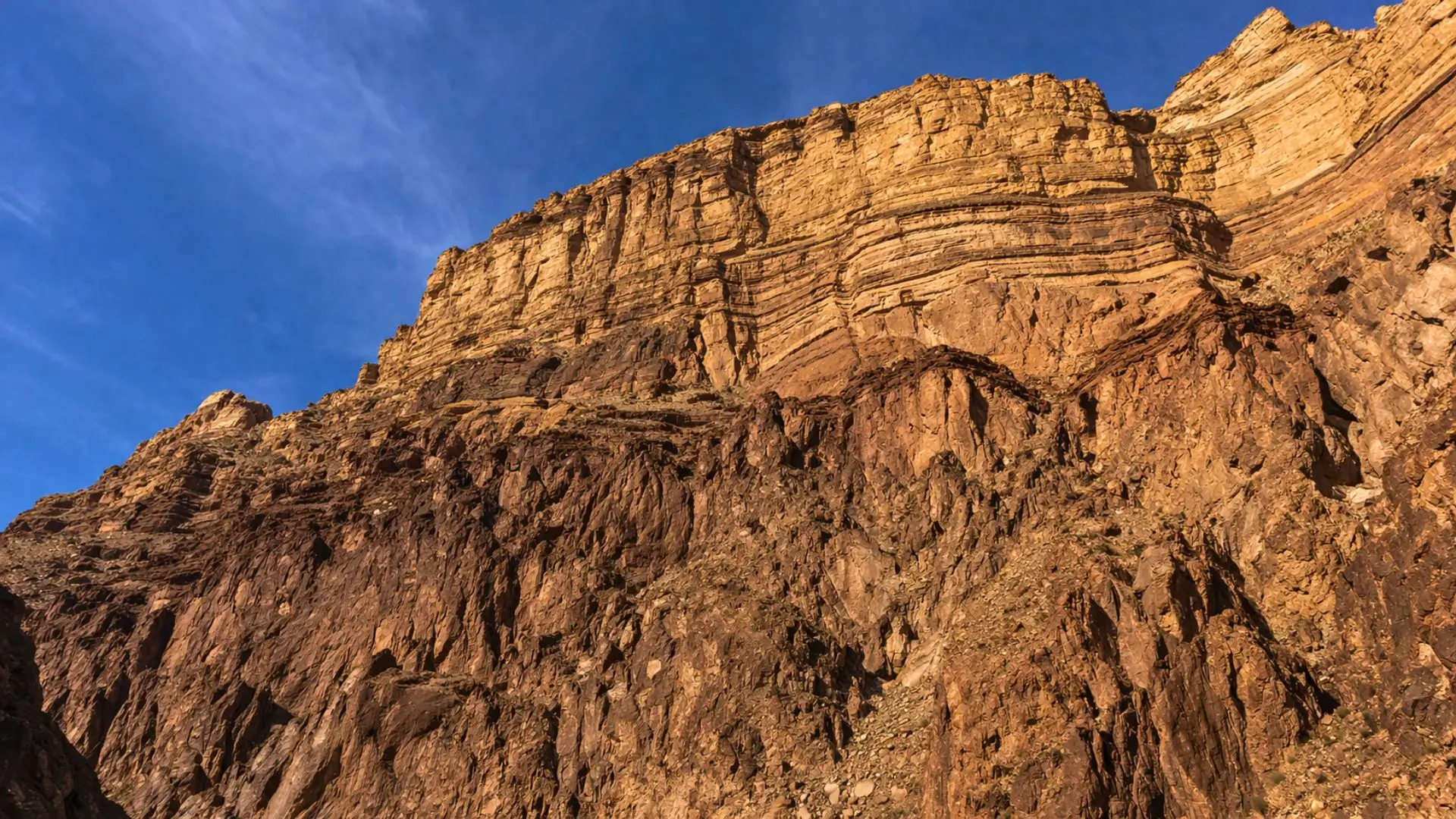 Vue spectaculaire depuis le fond du Grand Canyon vers d’immenses falaises stratifiées, où une nette ligne de discordance sépare des roches très anciennes de couches sédimentaires plus récentes, sous une lumière dorée de fin d’après-midi.