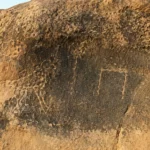 Inscriptions gravées sur une roche calcaire dans un wadi désertique d’Égypte ancienne, avec motifs d’oiseaux et symboles archaïques.