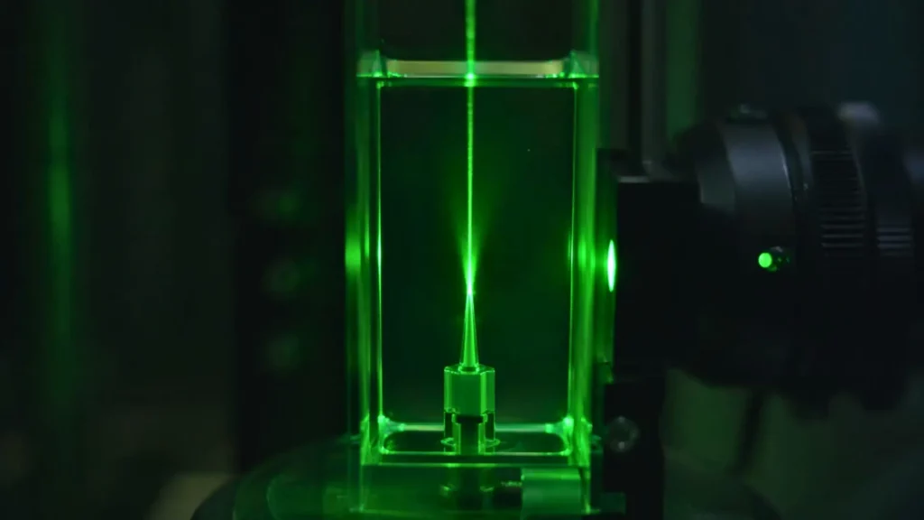 Structure métajet microscopique illuminée par un faisceau laser vert intense dans un environnement de test fluide propre.