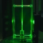 Structure métajet microscopique illuminée par un faisceau laser vert intense dans un environnement de test fluide propre.
