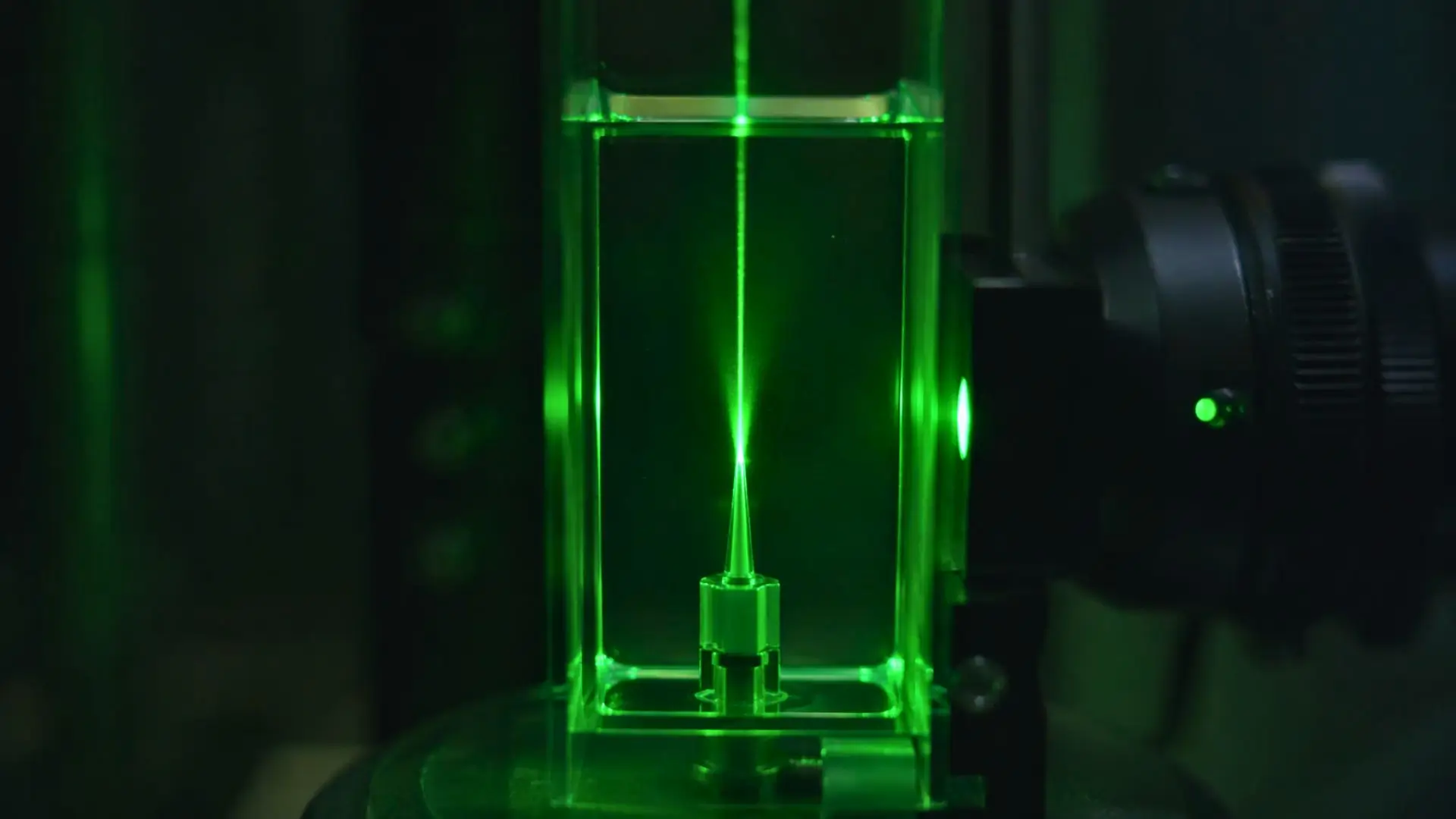 Structure métajet microscopique illuminée par un faisceau laser vert intense dans un environnement de test fluide propre.