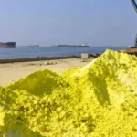 De vastes monticules de soufre jaune vif s’élèvent sur un quai industriel poussiéreux, face à des pétroliers immobiles sur une mer calme dans le détroit d’Ormuz.