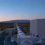 Un observatoire d’ondes gravitationnelles au crépuscule, avec de longs tubes à vide filant vers l’horizon sous un ciel clair parsemé de faibles étoiles.