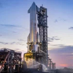 Une fusée Starship en acier inoxydable sur son pas de tir au Texas, au crépuscule, avec tour de lancement et infrastructures visibles.