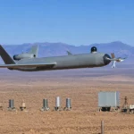 Drone militaire moderne avec lame frontale volant à basse altitude au-dessus d’un terrain d’entraînement désertique