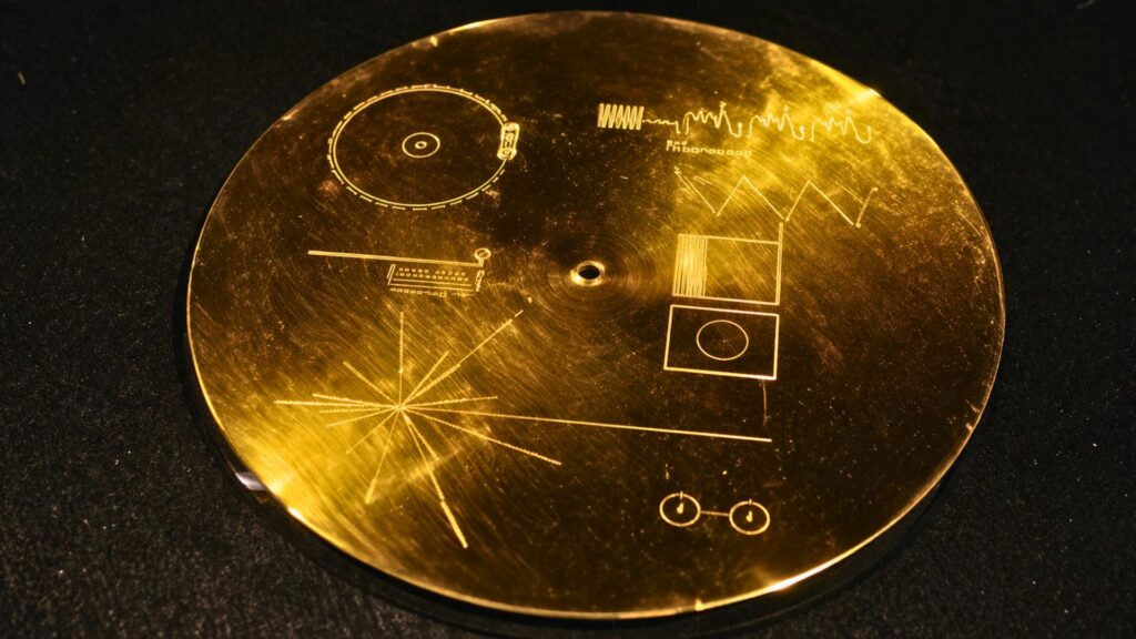 Gros plan photoréaliste du disque d’or de Voyager, posé sur une surface sombre, avec ses gravures scientifiques finement visibles et un reflet doré subtil.