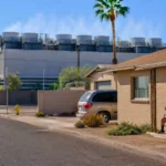 Quartier résidentiel de Phoenix situé près d’un grand data center, sous un soleil intense, avec un habitant assis à l’ombre devant sa maison.