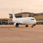 Avion blanc sans logo stationné sur un tarmac devant un terminal moderne.