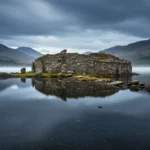 Île artificielle néolithique immergée dans un loch écossais avec ancien chemin de pierre sous l’eau et paysage des Highlands en arrière-plan.