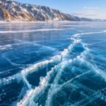 Glace bleue fissurée du lac Baïkal avec montagnes enneigées en arrière-plan.