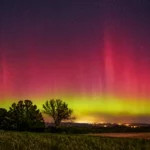 Aurore rouge et verte visible au-dessus d’un paysage rural français sous un ciel étoilé.