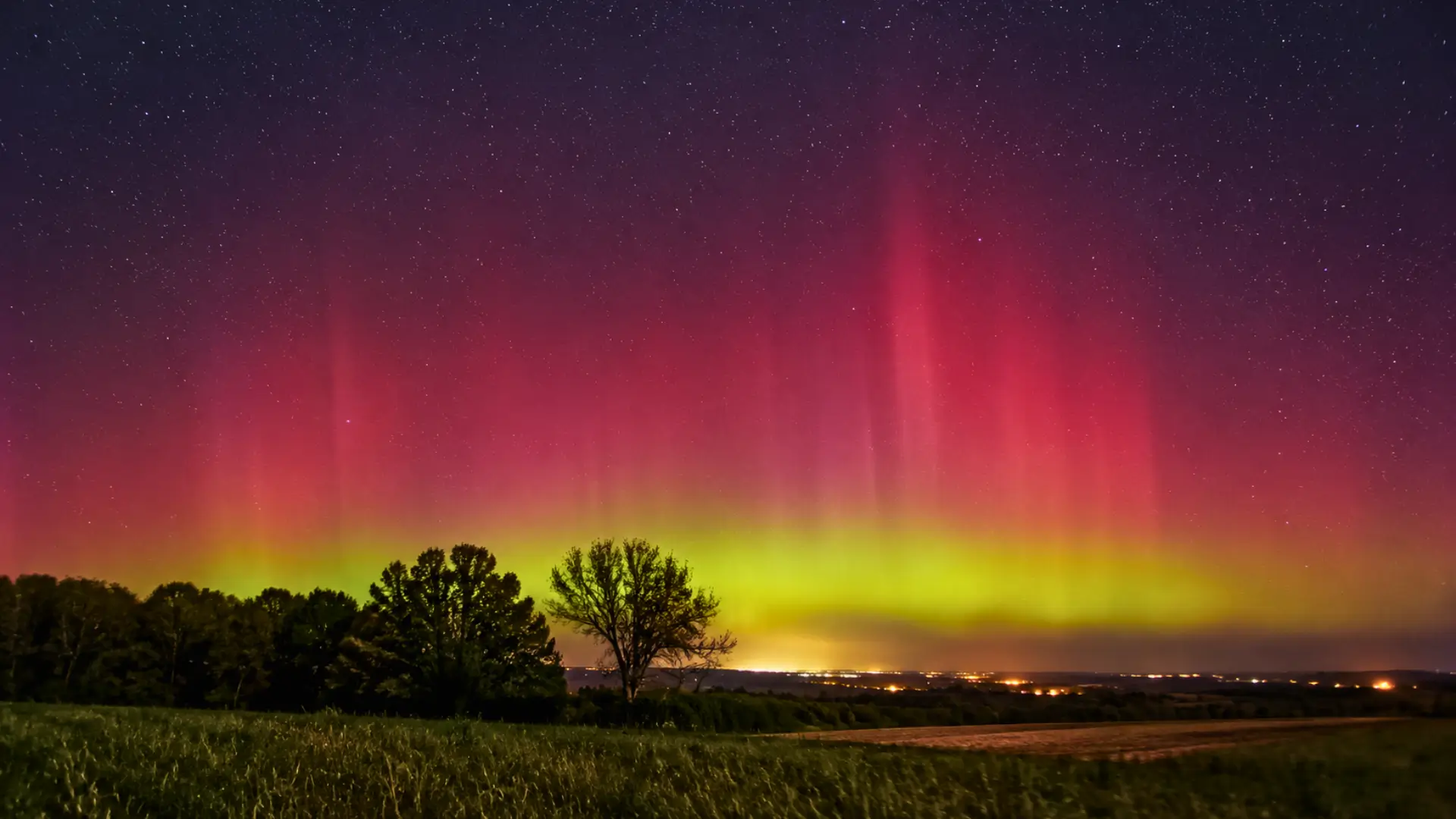 Aurore rouge et verte visible au-dessus d’un paysage rural français sous un ciel étoilé.