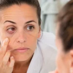 Femme fatiguée examinant une paupière irritée devant un miroir au réveil
