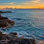 Littoral rocheux et océan au coucher du soleil, évoquant l’origine profonde de l’eau terrestre.