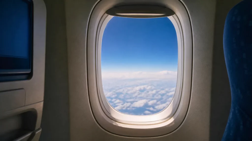 Hublot d’avion rond vu de l’intérieur avec ciel bleu et nuages à haute altitude