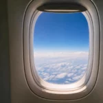 Hublot d’avion rond vu de l’intérieur avec ciel bleu et nuages à haute altitude