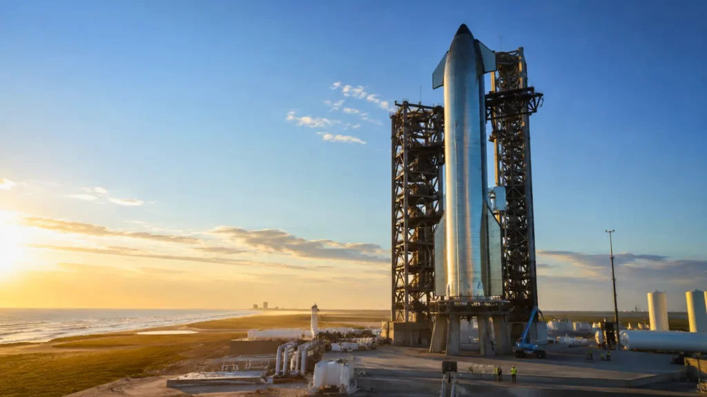 Le Starship de SpaceX dressé sur un pas de tir côtier au lever du soleil, entouré de structures industrielles et de techniciens.