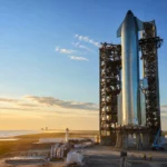 Le Starship de SpaceX dressé sur un pas de tir côtier au lever du soleil, entouré de structures industrielles et de techniciens.