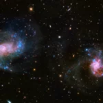 Deux galaxies lointaines brillent dans l’espace profond, entourées de gaz lumineux et d’étoiles, illustrant des trous noirs supermassifs observés par le télescope James Webb.