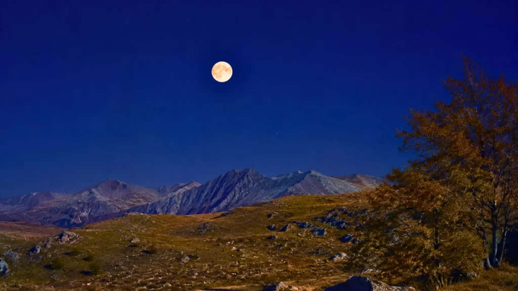 Pleine lune visible dans un ciel nocturne clair au-dessus d’un paysage montagneux, illustrant la lune bleue et microlune du 31 mai 2026.