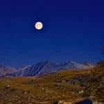 Pleine lune visible dans un ciel nocturne clair au-dessus d’un paysage montagneux, illustrant la lune bleue et microlune du 31 mai 2026.