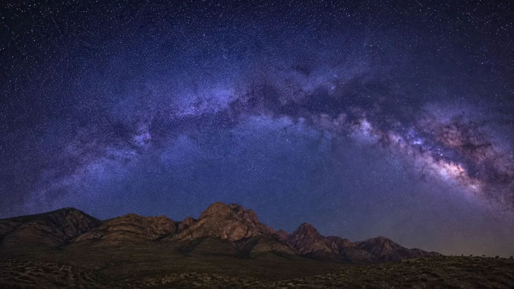 Voie lactée au-dessus de montagnes sombres sous un ciel étoilé profond.
