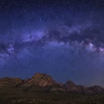 Voie lactée au-dessus de montagnes sombres sous un ciel étoilé profond.
