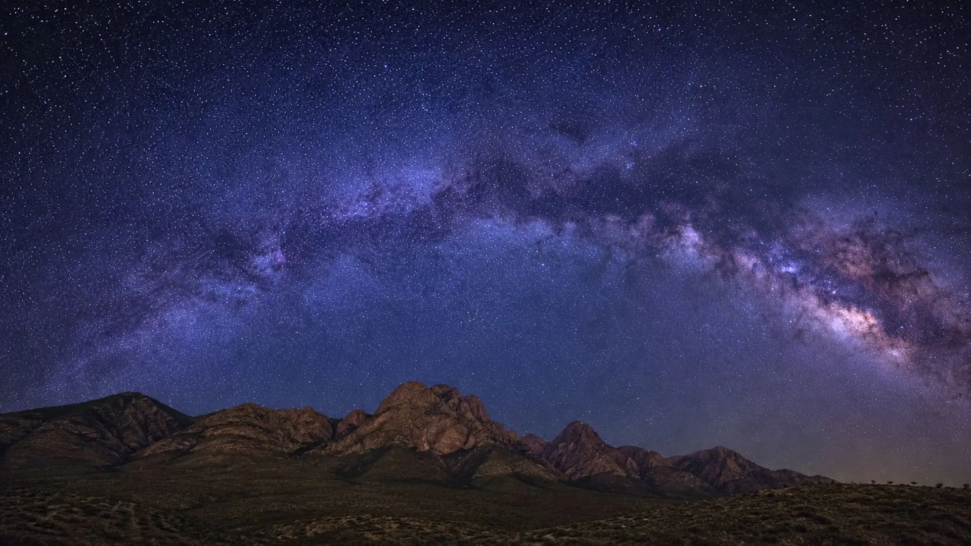 Voie lactée au-dessus de montagnes sombres sous un ciel étoilé profond.
