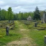 Vue réaliste d’un village déserté près de Verdun, avec des ruines en pierre, un chemin central et une forêt sous un ciel gris.