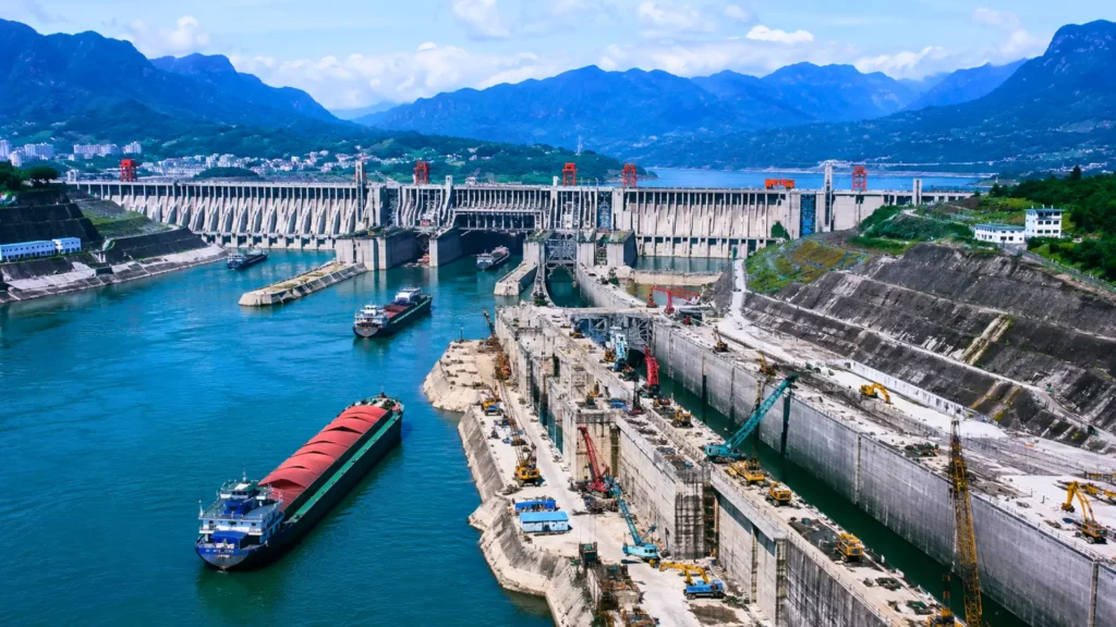 Vue aérienne réaliste du barrage des Trois-Gorges en Chine, avec des cargos naviguant sur le Yangtsé et un vaste chantier d’écluses.
