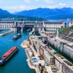 Vue aérienne réaliste du barrage des Trois-Gorges en Chine, avec des cargos naviguant sur le Yangtsé et un vaste chantier d’écluses.