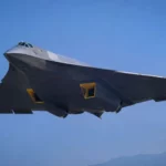 Un prototype de chasseur furtif chinois sans dérive verticale survole un ciel bleu, vu depuis le sol lors d’un vol d’essai.