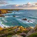 Littoral breton rocheux bordé par une mer agitée sous une lumière dorée.