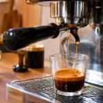 Espresso en cours d’extraction dans une tasse en verre sous une machine à café, dans une cuisine chaleureuse.