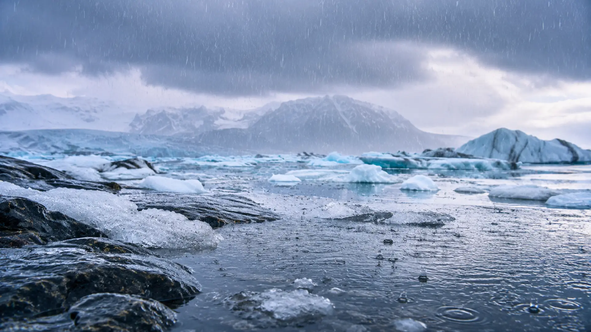 Pluie froide tombant sur une étendue glacée de l’Arctique avec des blocs de glace, de l’eau sombre et des montagnes sous un ciel couvert.