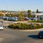 Rond-point paysager dans une zone commerciale française avec plusieurs voitures en circulation.