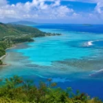 Vue panoramique du lagon turquoise de Mayotte, entouré de collines verdoyantes, de récifs coralliens et de l’océan Indien.